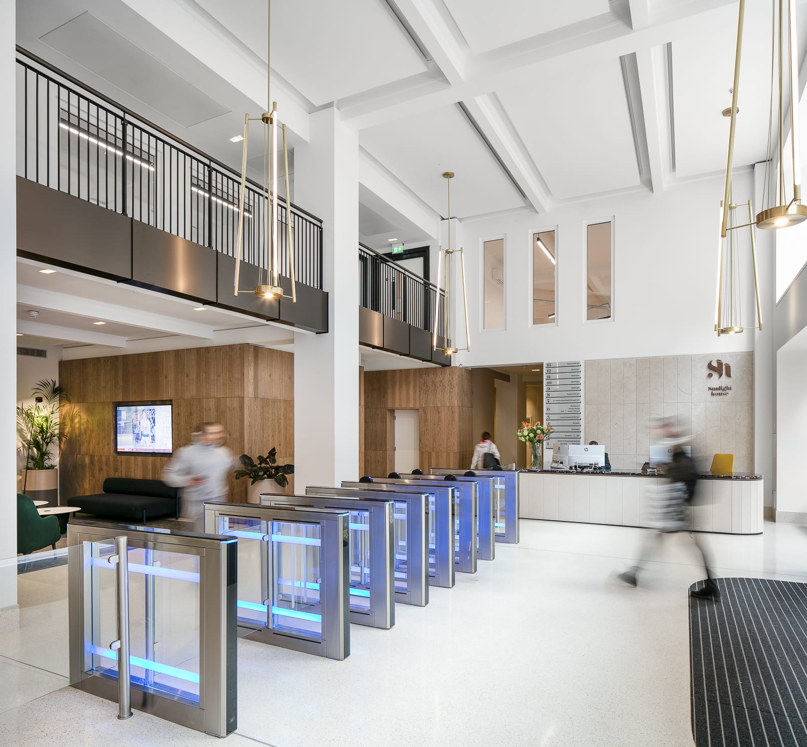 Modern office reception with suspended pendant lights, LED downlights, and illuminated security barriers.