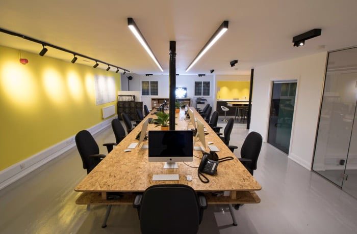 Office lighting design with linear overhead fixtures and wall-mounted track lights illuminating a modern shared workspace.