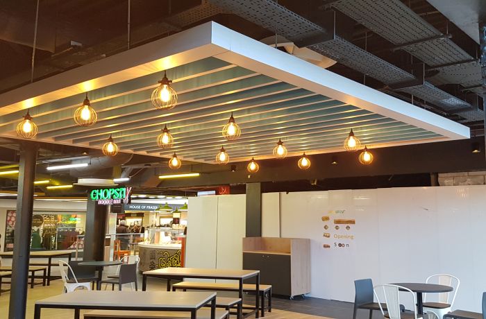 Food court seating area with a suspended ceiling panel featuring exposed filament cage lights