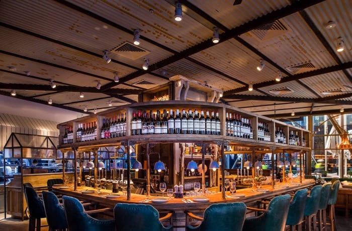 Restaurant bar with wine display, illuminated by ceiling-mounted track lighting and pendant lights.