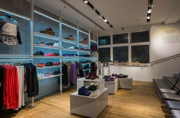 Retail store with track spotlights and integrated shelf lighting highlighting shoes and apparel displays.