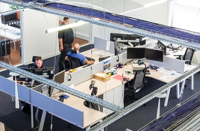 Modern open-plan office with suspended linear LED lighting providing bright, even illumination across workstations