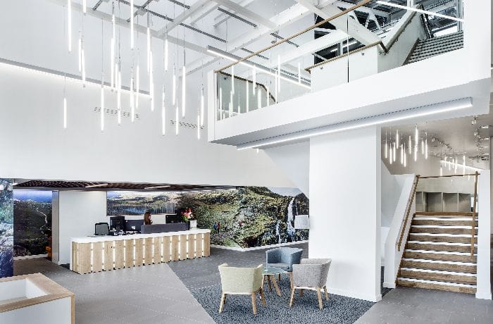 Modern office reception with suspended linear LED pendants and recessed ceiling lighting illuminating the space.