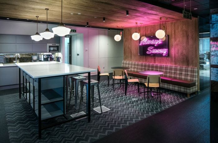 Office lighting design with pendant fixtures and neon signage in a modern breakout space.
