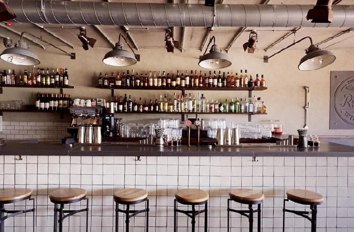 Bar lighting design with industrial ceiling lights illuminating a tiled counter and bottle display.